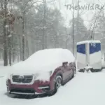 A custom-built RV and car covered in heavy snow during a winter photography expedition.
