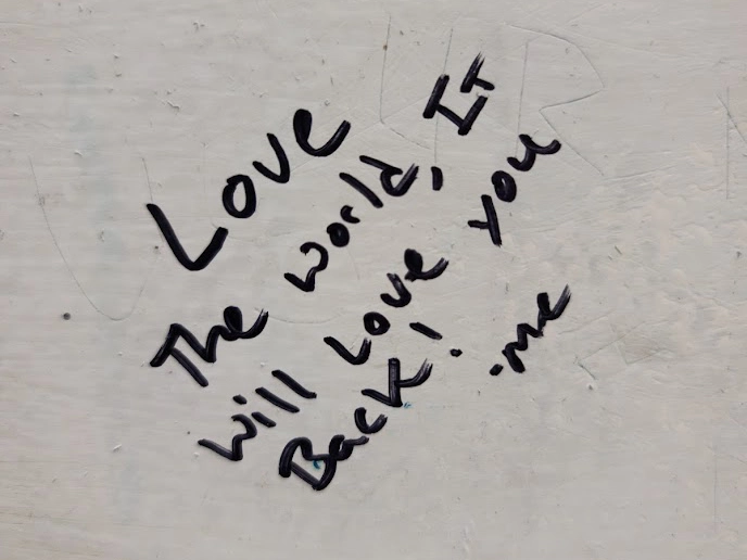 andwriting on a bathroom stall door in a Western USA rest stop that reads, "Love the world, it will love you back! - me."
