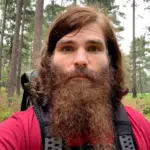A hiker wearing a well-adjusted backpacking pack on a scenic mountain trail, showing the correct position of the hip belt and shoulder straps.