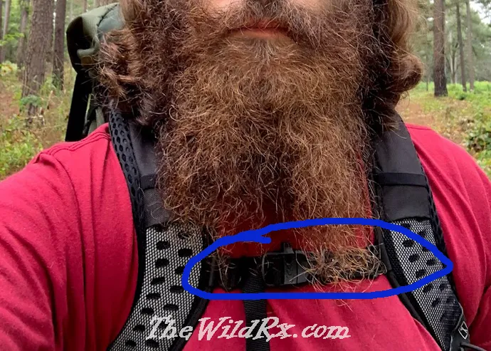 A close-up of a hiker wearing a backpack with a blue circle highlighting the sternum strap buckled across the chest at the correct height below the collarbone.