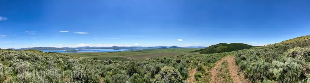 anoramic view of southeastern Idaho mountains overlooking a portion of Blackfoot Reservoir, featuring winding dirt riding trails and high-desert vegetation.