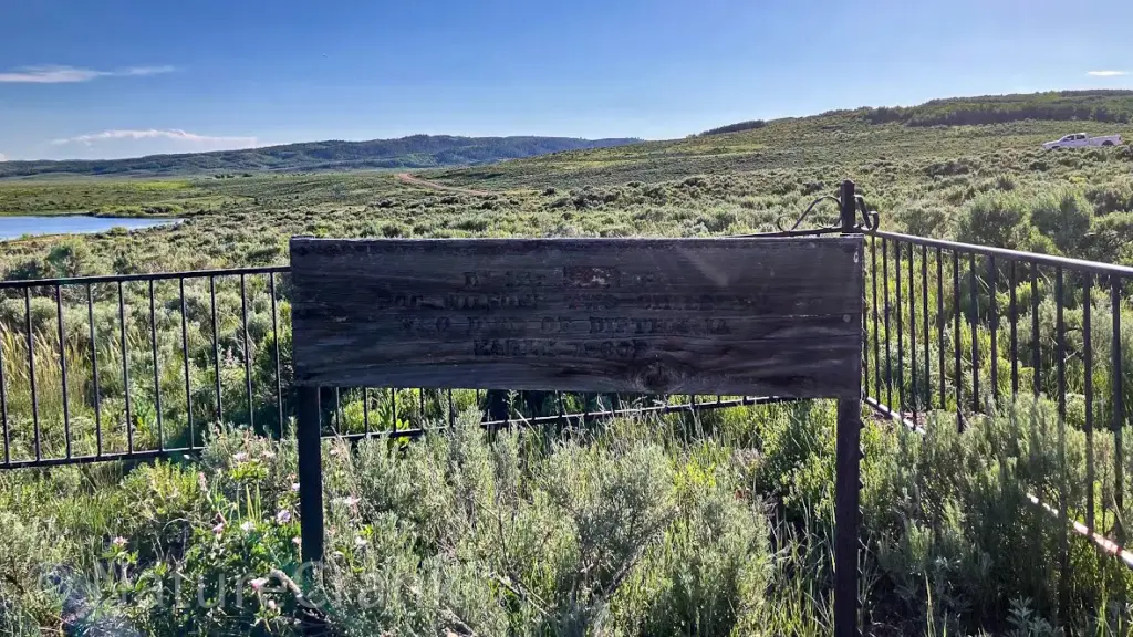 A weathered rectangular wooden sign at the Blackfoot Reservoir gravesite, with white text reading "In Memory of Doc Wilsons Two Children Who Died of Diptheria Early 1900's.