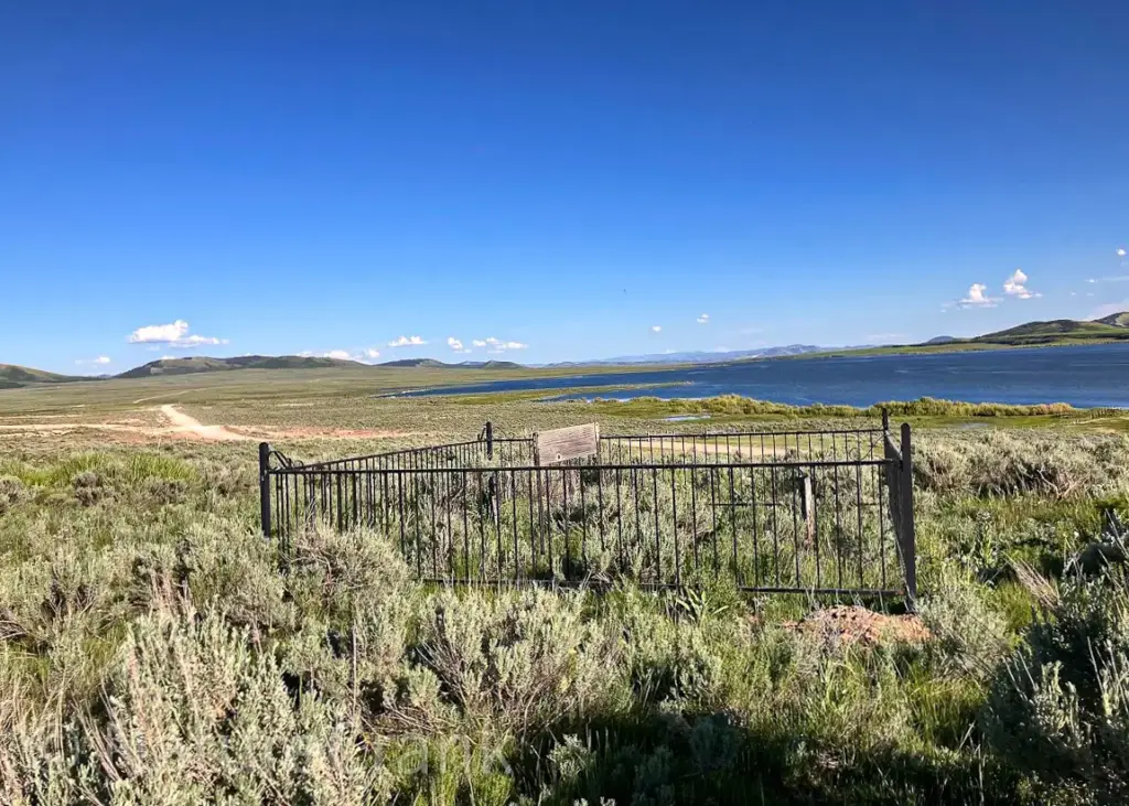 A wide-angle view of the Doc Wilson children's gravesite, showing the small fenced enclosure standing alone in the open Idaho desert landscape.