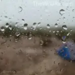Close-up of raindrops on an RV window with a blurred view of a remote campsite in the background.
