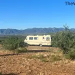 A cream-colored vintage motorhome parked in a dispersed camping spot in the northern Arizona high desert with blue mountains in the background.