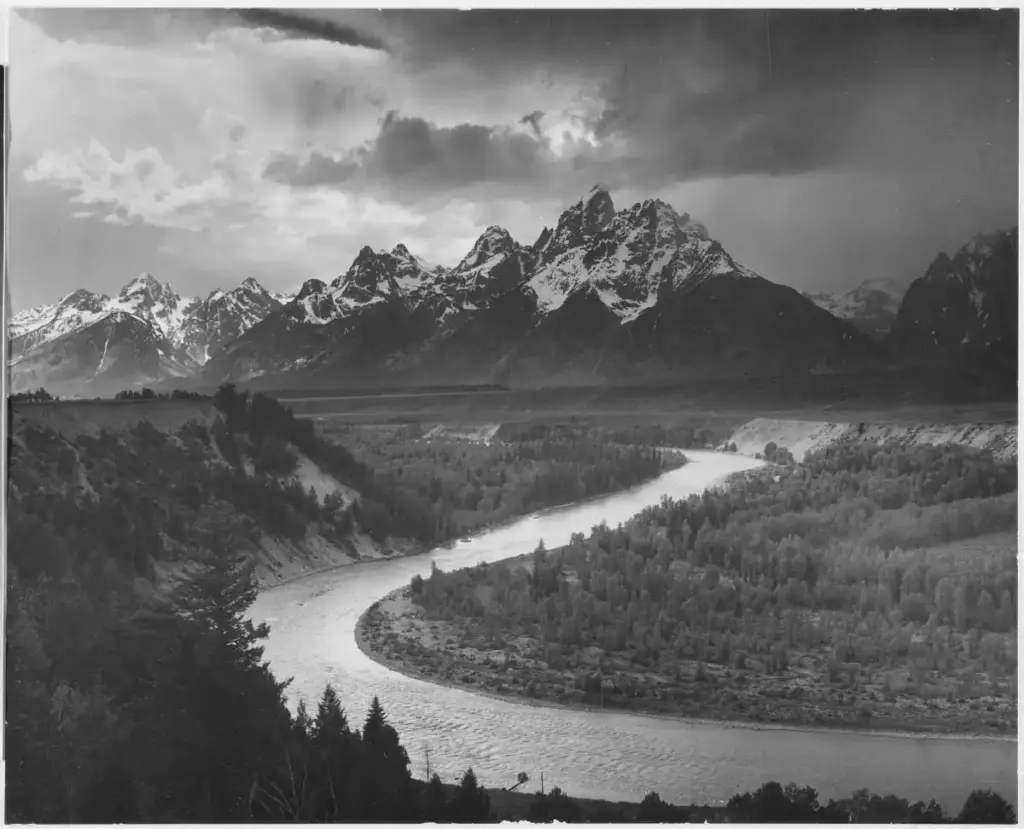 Famous black and white landscape photograph by Ansel Adams featuring the winding Snake River in the foreground and the snow-capped Teton mountain range under a dramatic storm sky.