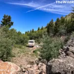 A Class A motorhome parked discreetly in a remote, rocky dispersed camping site surrounded by aspen trees and brush.