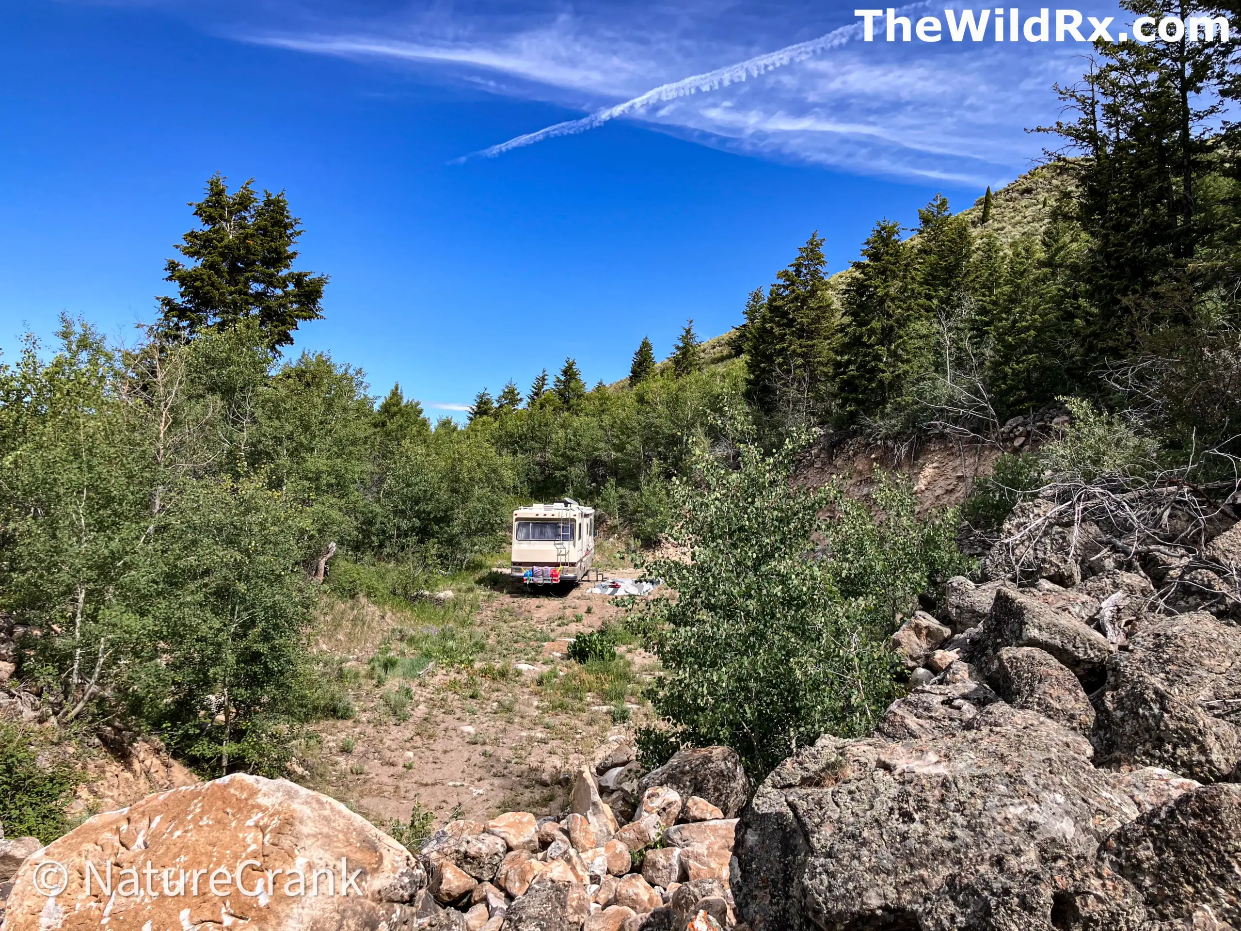A Class A motorhome parked discreetly in a remote, rocky dispersed camping site surrounded by aspen trees and brush.