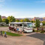 A family with children on bikes and a dog enjoying a stay at a Thousand Trails RV resort with a large Class A motorhome parked in a paved site.