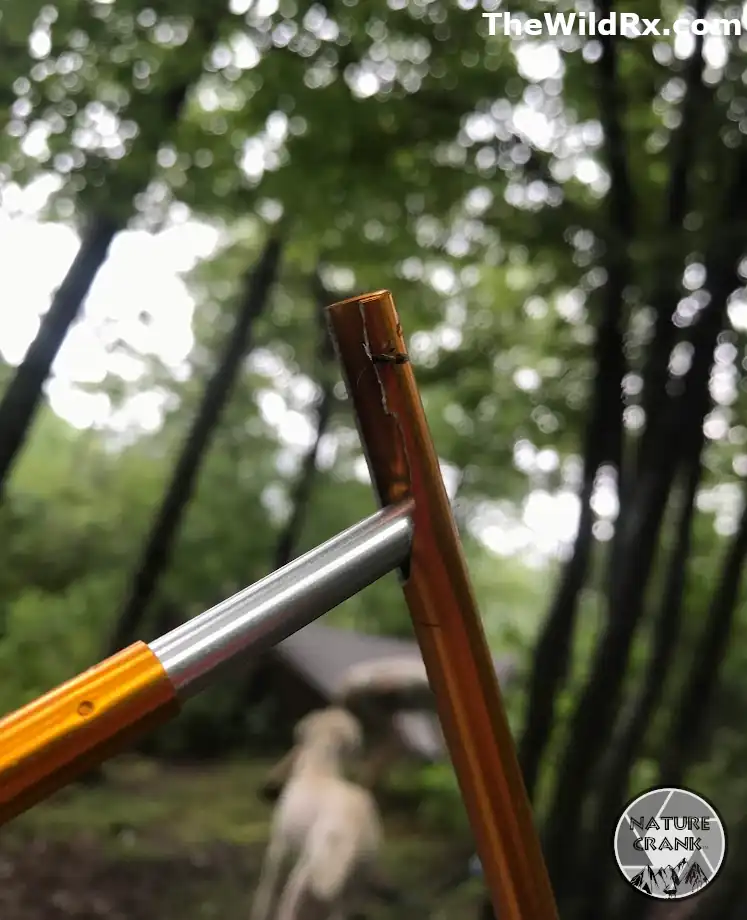 Close up of a split orange aluminum tent pole ferrule with a silver insert held up against a blurry forest background on the Appalachian Trail.