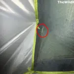 A close-up view from inside a tent showing a broken orange aluminum tent pole with a sharp, jagged fracture visible through the green mosquito mesh. The break is highlighted with a red circle.