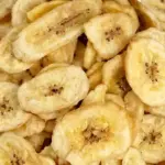 A close-up landscape view of crispy, golden dehydrated banana chips in a wicker basket, demonstrating the results of home food dehydration.
