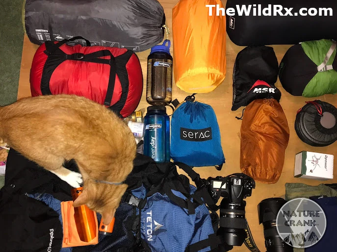 Side-by-side comparison of traditional backpacking gear versus lighter setup showing base weights, including a red sleeping bag, blue Teton backpack, orange tent, black MSR gear, titanium cookware, and camera equipment spread on the floor
