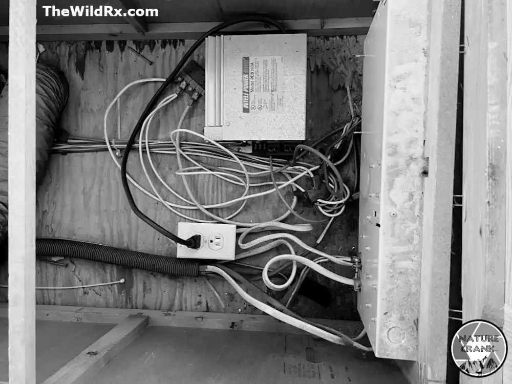 Black and white photo of an older RV electrical compartment featuring an Inteli-Power 9100 converter and tangled wires during a parasitic battery drain test.